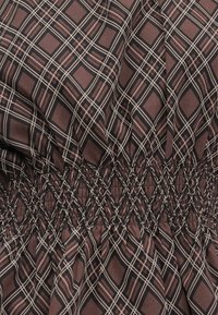 Brunt rutete stoff med en smocket design med svarte og lyserosa linjer, som skaper et teksturert, rynket utseende.