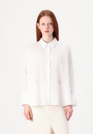 White button-up shirt made of lightweight fabric, featuring cut-out heart designs. It has a spread collar and long sleeves with cuff details.