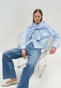 Gestreifte hellblaue Hemd mit Kragen und einer passenden Krawatte über die Schultern drapiert, kombiniert mit hellblauen, weit geschnittenen Jeans und beigen Ballerinas.