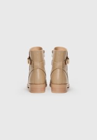 Bottines en cuir beige avec un bout arrondi, une fermeture éclair sur le côté et un petit talon empilé. Présente des coutures croisées et une boucle décorative.