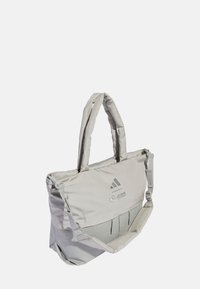 Grå stofnet med polstrede håndtag, justerbar rem, frontlomme og trykte logoer. Har en slank rektangulær form.