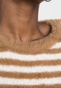 Gestreifter Pullover in Braun und Weiß mit einer weichen, flauschigen Textur, rundem Ausschnitt und sichtbaren Nähten entlang der Kanten.