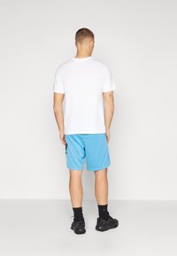 Bela majica s okruglim izrezom, modre kratke hlače s logotipom sa strane, crne čarape i crne sportske tenisice. Fokus na dizajn ležerne sportske odjeće.