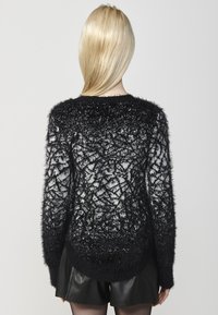 Maglione fuzzy bianco e nero con motivo texturizzato, maniche lunghe, scollatura rotonda e orlo leggermente allungato. Indossato con pantaloncini neri.