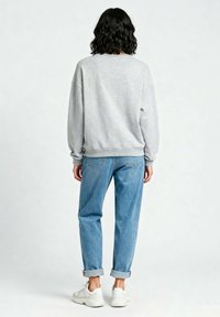 Felpa grigia con spalle scese, orlo e polsini a costine; abbinata a jeans azzurri con risvolto e scarpe da ginnastica bianche.