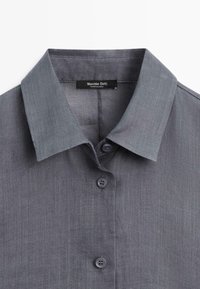 Szary kołnierzyk koszuli zapinanej na guziki z trzema widocznymi guzikami oraz metką "Massimo Dutti" przyszytą wewnątrz dekoltu.