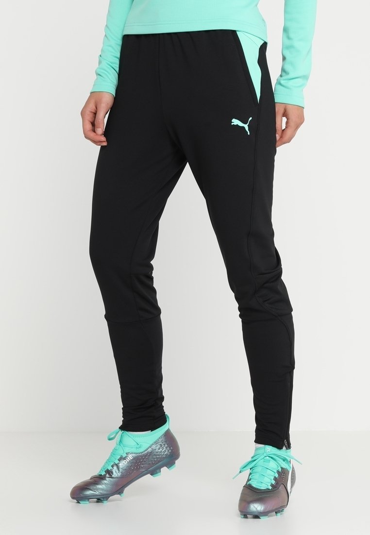 Svarta träningsbyxor med en tajt passform, utrustade med sidofickor och en ljusblå Puma-logotyp. Matcher med matchande turkosa fotbollsskor.
