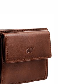 Cartera de cuero marrón con una superficie texturizada, que presenta un cierre de solapa y un logo en relieve. La costura en los bordes es visible, realzando el detalle del diseño.