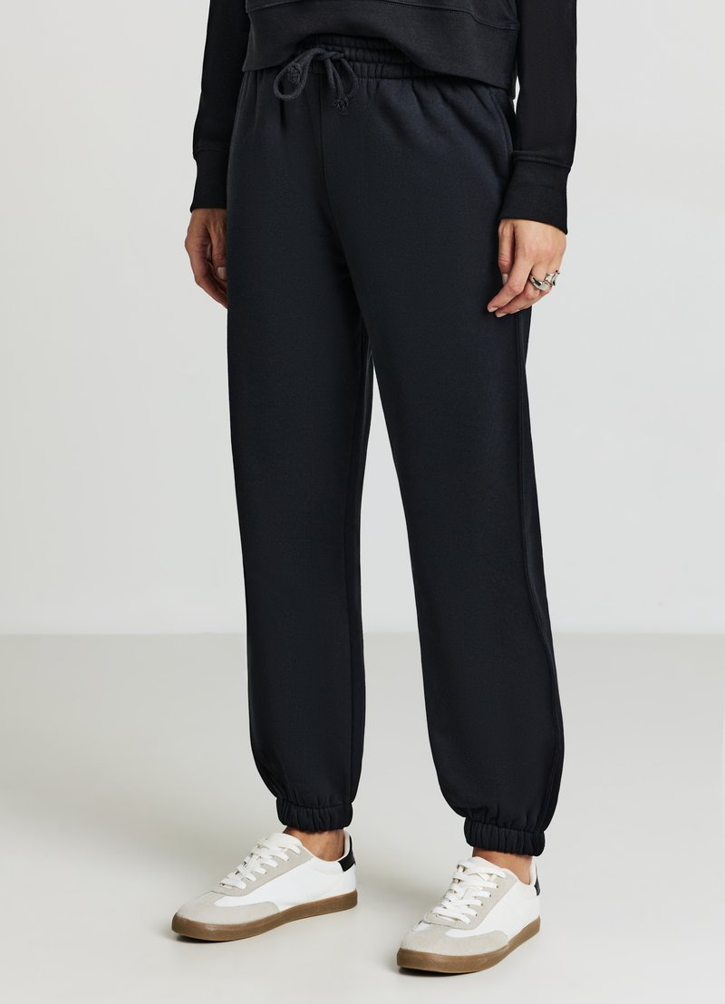 Pantaloni sportivi neri con cintura elastica e polsini, realizzati in tessuto morbido. Abbinati a scarpe da ginnastica bianche e grigie con accenti testurizzati.