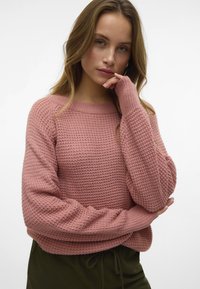 Pull en tricot rose avec un motif texturé, des manches larges et une coupe ample. Il présente des poignets côtelés et un col rond.