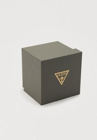 Crna teksturirana poklon kutija sa zlatnim trokutastim logotipom sprijeda, s imenom marke "GUESS" i ukrasnim elementima.