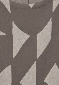 T-shirt en tissu cotonnade présentant un motif abstrait crème et marron. Le design inclut de grandes formes avec une apparence texturée et mélangée.