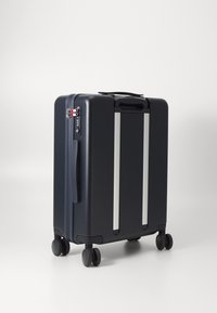 Valigia rigida blu navy con superficie testurizzata, accenti argentati, serratura a combinazione e quattro ruote nere per la mobilità.