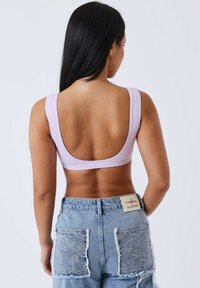 Top corto lila con espalda baja y tirantes anchos, combinado con pantalones cortos de mezclilla azul de tiro alto con bolsillos de encaje.