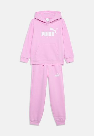 Chándal Puma de color rosa claro con capucha y pantalones a juego, con el logo blanco de Puma en el pecho y el muslo izquierdo.