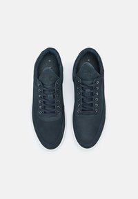 Paire de baskets bleu marine à lacets avec semelles blanches, vues de dessus sur un fond clair uni.