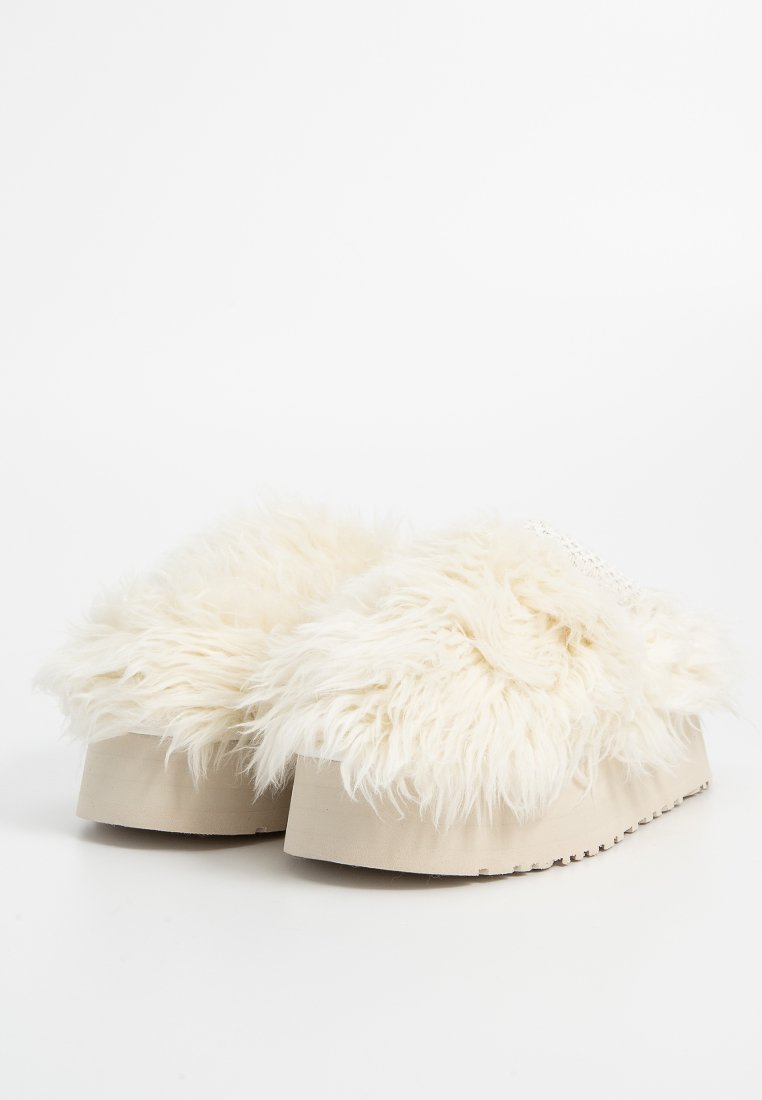 Un paio di pantofole con piattaforma beige ricoperte di fitta e soffice pelliccia bianca, su uno sfondo bianco semplice.