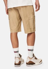 Beige cargo shorts med to sidelommer, parret med hvide sokker med røde og grønne striber og beige sneakers med teksturerede accenter.
