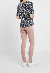 Haut à manches courtes navy avec un motif léopard multicolore, associé à un jean skinny rose pastel et des baskets blanches.