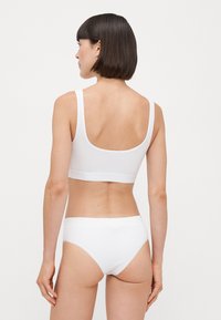 Valkoinen puuvillainen bralette, jossa on leveät hihnat ja syvä selkäosa, yhdistettynä vastaaviin matalavyötäröisiin alushousuihin, joissa on pehmeä vyötärönauha ja saumatonta muotoilua.