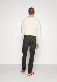 Černé džíny z denimu, slim fit, s vybledlým povrchem. Nohavice jsou kombinovány s krémovou košilí s dlouhým rukávem a vícebarevnými teniskami, pohled zezadu.