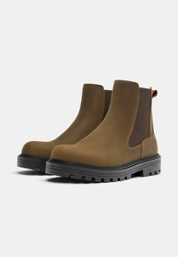 Hnedé členkové topánky z semišu s elastickými bočnými panelmi, okrúhlou špičkou a robustnou čiernou gumovou podrážkou s textúrovaným vzorom dezénu.