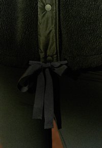 Czarna polarowa kurtka z gładką podszewką wewnętrzną, związywana wstążką w talii, zapinana na okrągłe czarne guziki.