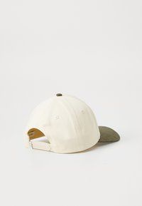 Baseball cap with a cream fabric body and green suede brim. Includes a snapback closure, visible stitching, and a top button.