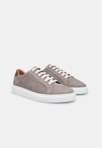 Zapatillas gris claro con piel lisa y perforada, suela de goma blanca y cordones blancos. Presentan una puntera redondeada y un diseño minimalista.