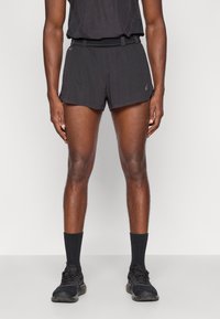 Μαύρες αθλητικές βερμούδες με υφή, ελαστική μέση και πλαϊνές σχισμές. Συνδυασμένες με μαύρες κάλτσες και αθλητικά παπούτσια.