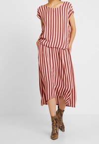 Conjunto de dos piezas a rayas que incluye una blusa suelta y una falda a juego, en colores óxido y crema. Tejido ligero con bolsillos laterales. Botas con patrón de pitón.