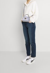 Light gray crossbody bag with a structured shape, gold hardware, and a textured surface. Paired with a cream knit sweater and dark jeans.