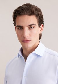 Lichtblauw overhemd met knopen en een gestructureerde stof, voorzien van een spitse kraag en een enkele borstzak, afgebeeld op een neutrale achtergrond.