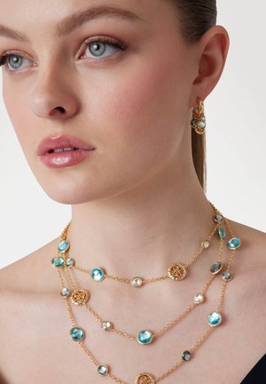 Goudvergulde sieradenset met gelaagde kettingen met blauwe en heldere kristallen, versierd met ronde gouden medaillons en bijpassende oorbellen.