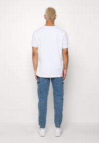 Camiseta blanca de algodón con mangas cortas, combinada con pantalones cargo azules que cuentan con bolsillos, puños elásticos y un ajuste relajado.