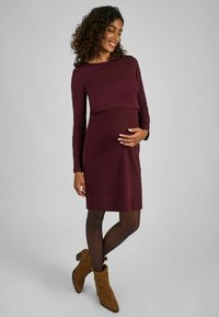 Burgundy ribbed raskausmekko, jossa on pitkät hihat, istuva yläosa ja rento hameosa, yhdistettynä ruskeisiin nilkkakorkokenkiin.