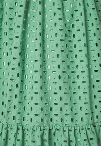 Tejido verde con un diseño texturizado que presenta cortes ovalados, terminado con un dobladillo rizado, creando una apariencia en capas.