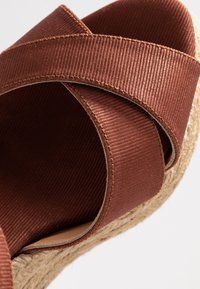 Hnědé látkové křížové popruhy na juteové platformě, která má hladký povrch a jemnou vroubkovanou strukturu.