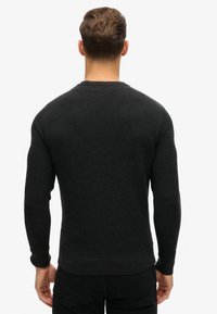 Svart texturerad tröja med ribbat mönster. Har långa ärmar och rund halsringning. Åtsittande mudd och midja.