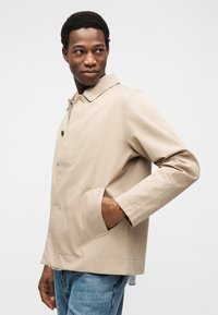 Μπεζ ελαφρύ μπουφάν με γιακά, κλείσιμο με κουμπιά και πλαϊνές τσέπες. Διαθέτει λείο ύφασμα και μίνιμαλ σχεδιασμό.