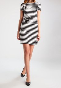 Černobílé pruhované šaty s krátkým rukávem a přiléhavým střihem, kulatým výstřihem a bočními kapsami, doplněné černými lodičkami s špičatou špičkou.