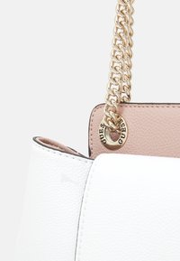 Vit texturerad läderhandväska med en rosa inre panel, guldkedjesnodd trätt genom en guldring graverad med "GUESS."