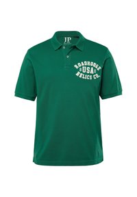 Zelená polo košile z bavlny s klasickým límcem, kterou zdobí přední potisk s textem "ROadhouse USA Relics Co." v bílé barvě.