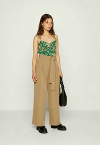 Top verde floral sem mangas com alças finas, combinado com calças largas de cintura alta em tom bege. Inclui sapatos pretos robustos e uma bolsa preta.