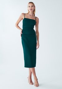 Smaragdově zelené midi šaty s přiléhavým, nařaseným živůtkem, tenkými ramínky a hladkou texturou látky. Kombinované s tělovými páskovými podpatky.