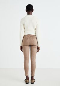 Krämfärgad stickad tröja, bruna sammetspants och skor med djurmönster. Ensemblet har tajta och texturerade element, sett bakifrån.