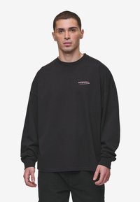 Schwarzer Langarm-Sweatshirt mit Rundhalsausschnitt, versehen mit einem kleinen, mehrfarbigen Logo auf der Brust. Hergestellt aus weichem Material mit lockerer Passform.
