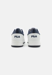 Fila sporta apavi ar baltu ādas virsu, tumši zilu akcentu, plakanu gumijas zoli un logotipa detaļām uz papēža un sāniem.
