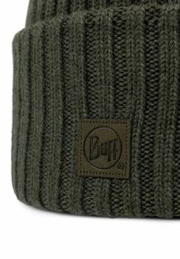 Dark green knitted beanie with vertical ribbed pattern and a brown leather logo patch featuring the "Buff" brand name. Soft texture.