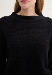 Schwarzer, strukturierten Pullover mit weitem Ausschnitt und weichem, mehrlagigem Stoff. Das Design ist schlicht, ohne sichtbare Muster oder Beschläge.